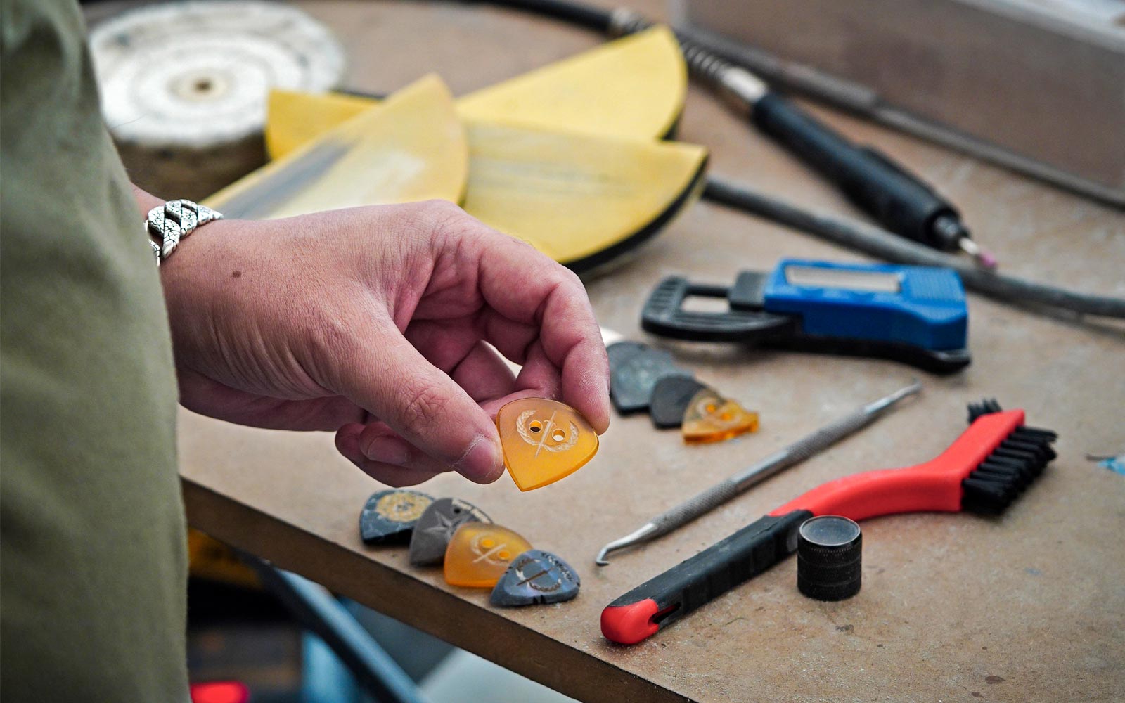 Iron Age Alex holding an handcrafted ultem guitarpick, workbench in background with other plectrums and tools
