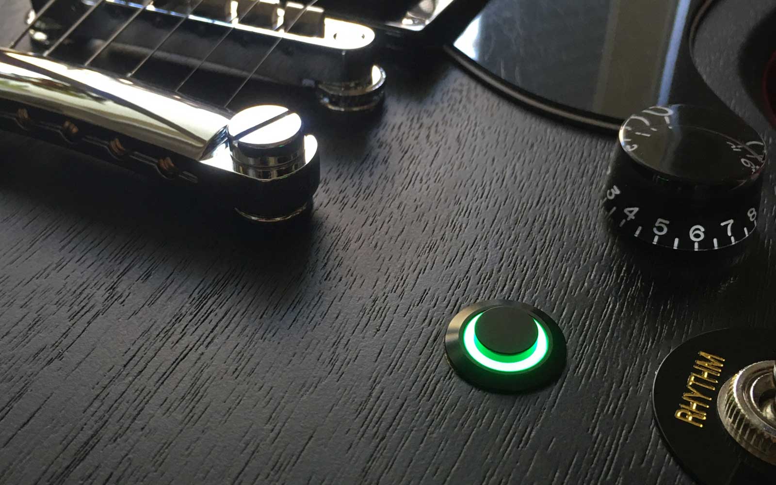 Black guitar kill switch with green LED ring installed on an electric guitar body