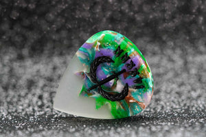 Colorful guitar pick with abstract design on a dark textured background