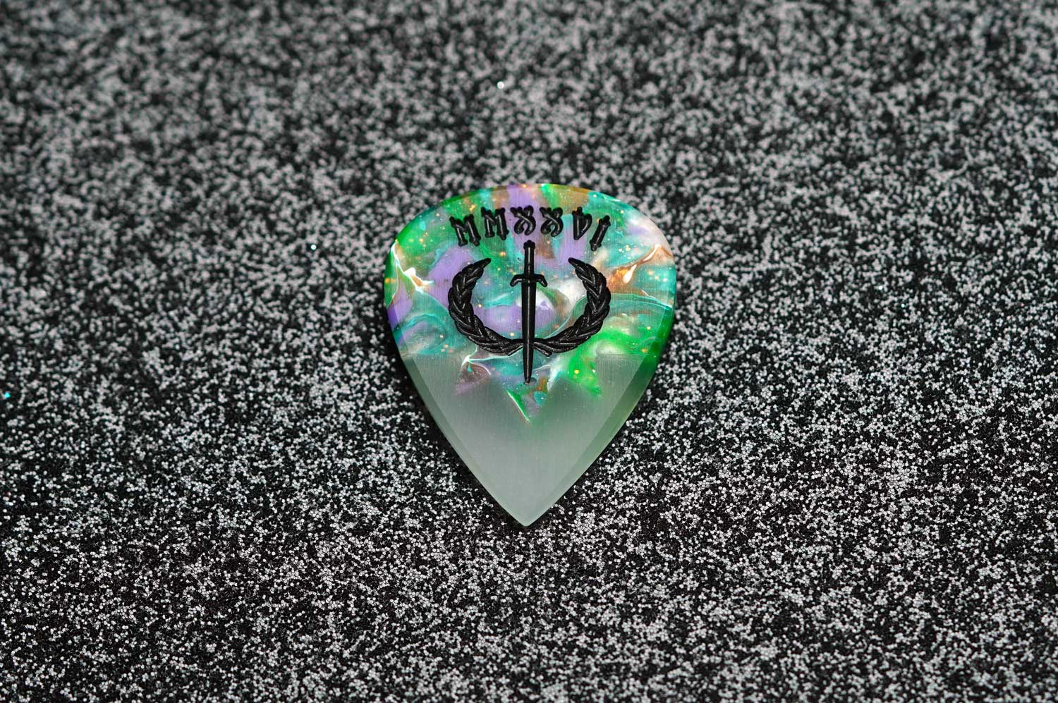 Glowing guitar pick with intricate design on a textured black surface
