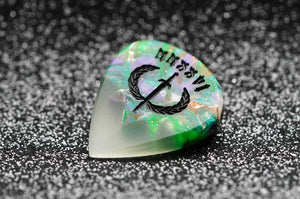 Opal guitar pick with engraved design on a dark textured background
