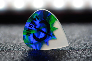 Guitar pick with a blue, green, and white design on a dark surface