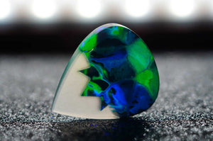 Colorful guitar pick with blue and green design on a dark surface