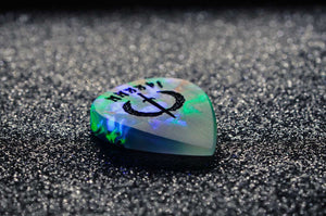 Opal like guitar pick with a symbol on a dark textured surface