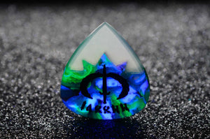 Teardrop-shaped resin guitar pick with a symbol and text on a dark textured background