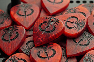 Batch of handmade Sol Invictus red resin plectrums showing natural variation in color and figure