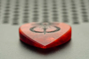 Close-up of the Sol Invictus guitar pick point and hand-finished bevels in red resin