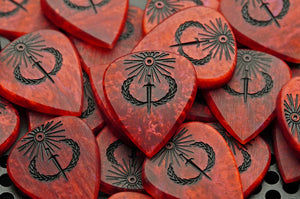 Limited run of finished Sol Invictus red resin guitar picks with black-filled solar engravings
