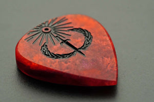 Thick Sol Invictus red resin guitar pick shown from a low angle with satin finish and engraved design